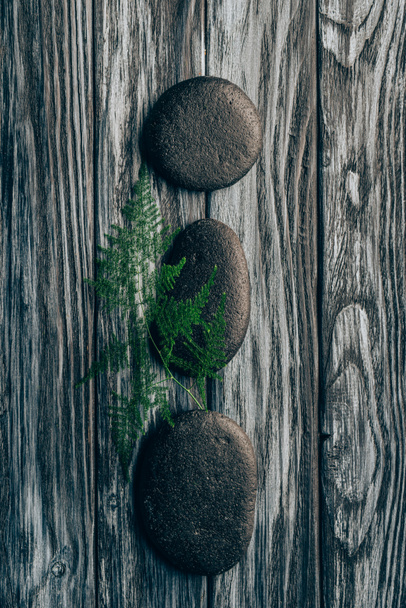top view of arranged fern and black pebbles for massage and spa on wooden background - Foto, immagini