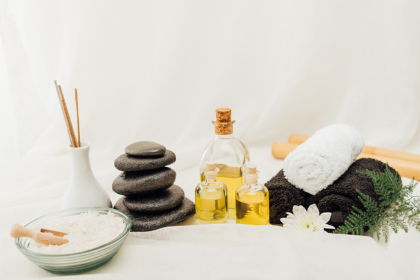 close up view of arrangement of spa treatment accessories with towels, pebbles and essential oil on white background - Photo, Image