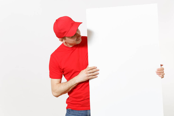 Levering jongeman in rood uniform geïsoleerd op een witte achtergrond. Mannelijke courier in GLB, t-shirt houden grote leeg Witboek billboard. Kopieer de advertentie ruimte. Plek voor tekst beeld. Gebied van de reclame - Foto, afbeelding