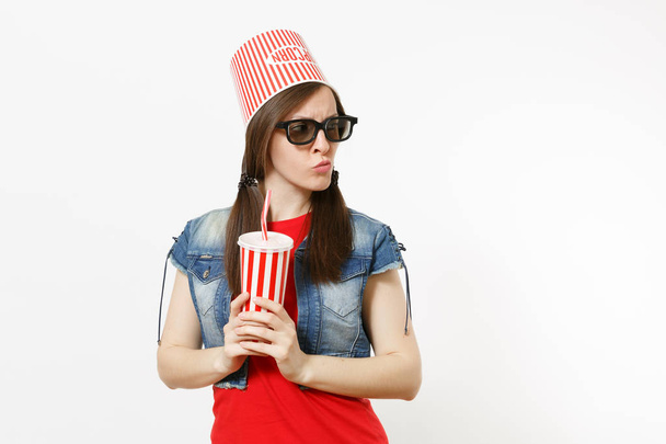 Ritratto di giovane donna carina interessata in occhiali 3d con secchio per popcorn sulla testa guardando film e tenendo in mano tazza di plastica di soda o cola isolata su sfondo bianco. Emozioni nel cinema
 - Foto, immagini