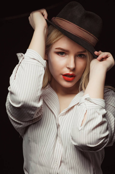 Nahaufnahme Porträt eines wunderbaren blonden Mädchens mit Brille und Hut, das mit dramatischem Licht im Studio posiert - Foto, Bild