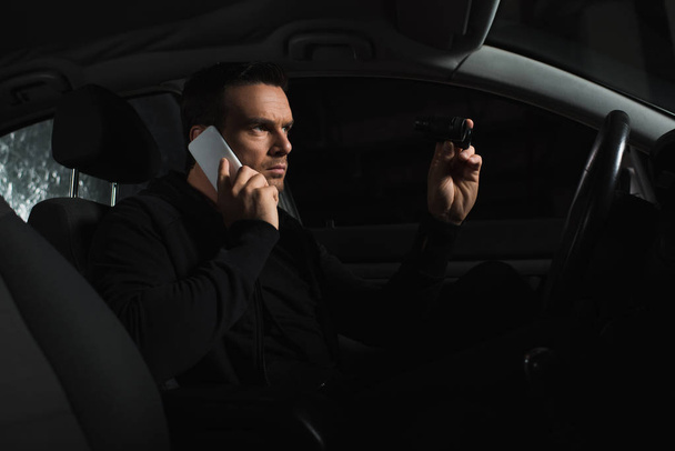 agente maschio sotto copertura concentrato che sorveglia con binocoli e parla su smartphone in auto
  - Foto, immagini