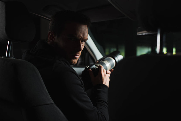 серьезный мужчина-папарацци смотрит в камеру во время наблюдения из машины
 - Фото, изображение