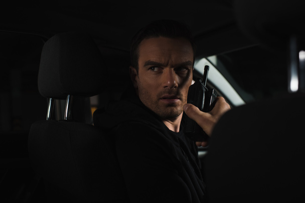 poważny mężczyzna prywatny detektyw za pomocą talkie walkie w samochodzie - Zdjęcie, obraz