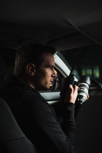 vista lateral de paparazzi macho haciendo vigilancia por cámara y usando walkie talkie en el coche
 - Foto, imagen