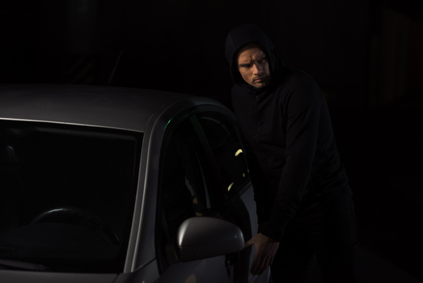focused male thief in black hoodie intruding automobile  - Photo, Image