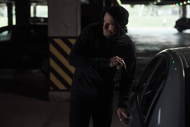 cautious male thief in black hoodie intruding car by picklock  - Fotoğraf, Görsel