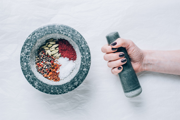 cropped image of woman holding pestle near mortar with spices on white table - Photo, Image