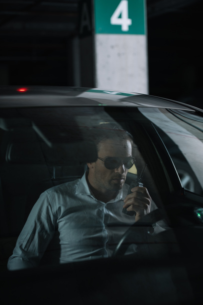 male undercover agent in sunglasses doing surveillance and using talkie walkie in car - Φωτογραφία, εικόνα