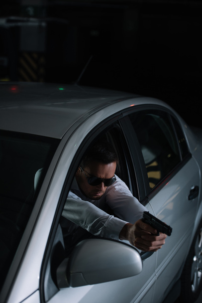 high angle view of male undercover agent in sunglasses aiming by gun from car - 写真・画像