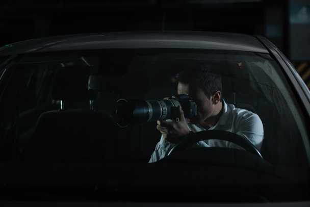 male private detective spying by camera with object glass from his car - Photo, Image