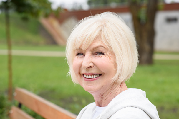 portrait of cheerful senior woman sitting on bench in park  - Photo, Image