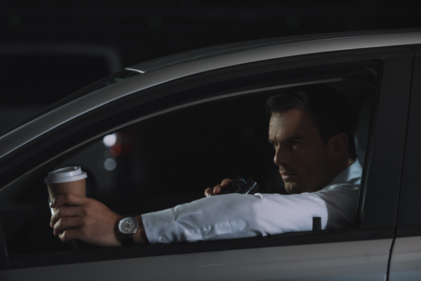 male undercover agent with paper cup of coffee using talkie walkie in car  - Fotoğraf, Görsel