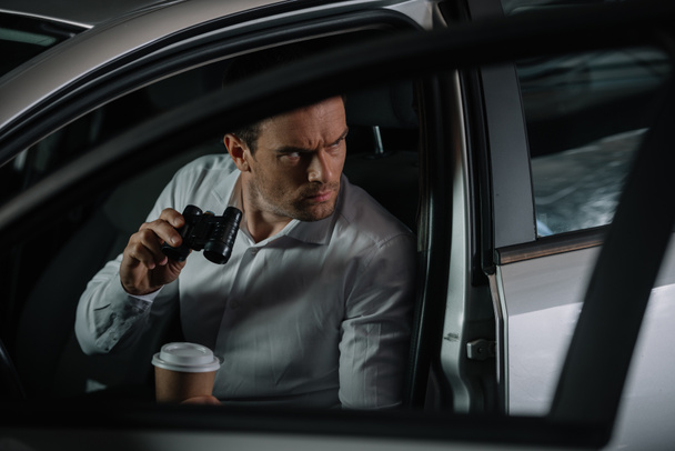 концентрований під прикриттям чоловічий агент, який здійснює спостереження біноклями та п'є каву в
 - Фото, зображення