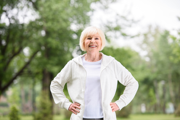 sonriente deportista de edad avanzada de pie en el césped verde en el parque
 - Foto, Imagen
