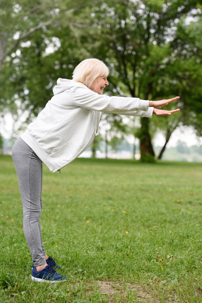 elderly sportswoman exercising on green grass in park, healthy lifestyle - Photo, Image