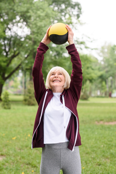 elderly sportswoman exercising with medicine ball in green park - Foto, Imagen