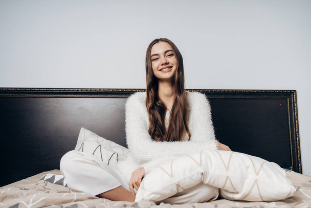 happy young girl in pajama sits in bed early in the morning, in good mood, smiling - Foto, Imagem