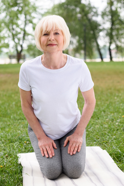 senior woman practicing yoga on mat on green lawn - Foto, Imagem