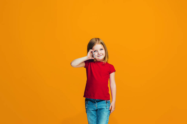 The happy teen girl standing and smiling against orange background. - Foto, afbeelding