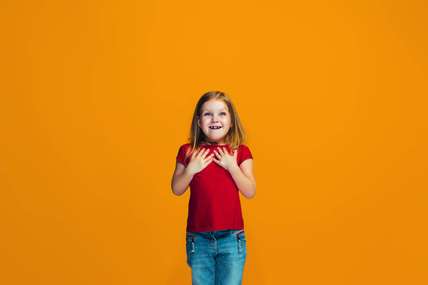 Щаслива дівчина-підліток стоїть і посміхається на помаранчевому фоні
. - Фото, зображення