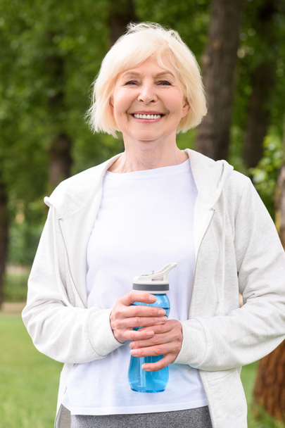 smiling senior sportswoman holding water in sport bottle    - Фото, изображение