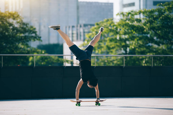 Skateboarder practicing handstand on skateboad at city - Fotó, kép