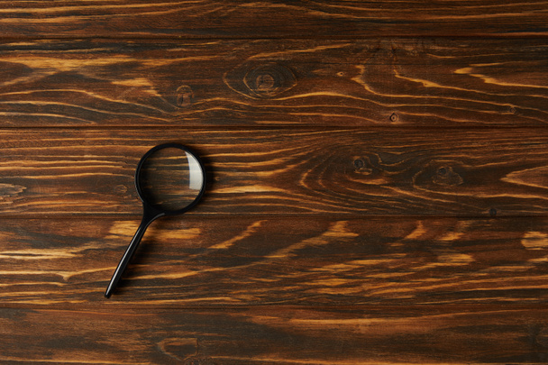 top view of single black magnifying glass with handle on wooden table - Photo, Image