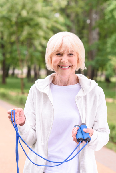 smiling senior sportswoman with skipping rope in park - Foto, afbeelding