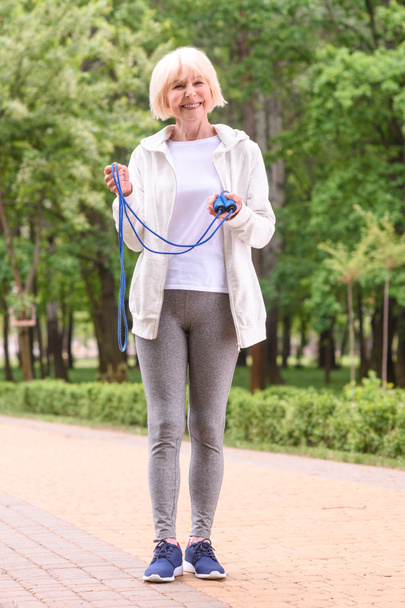 alegre deportista de edad avanzada de pie con cuerda de salto en el parque
  - Foto, imagen