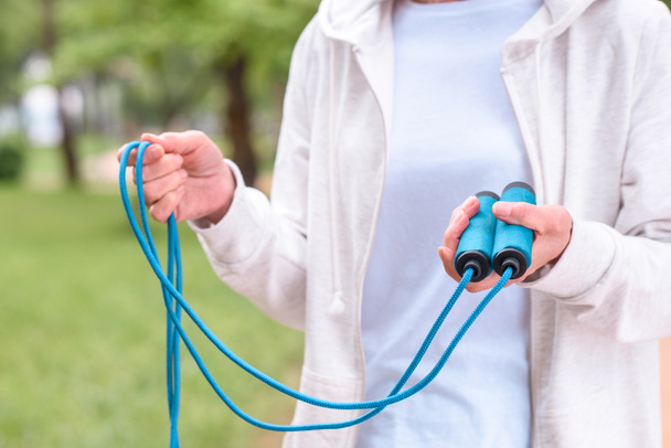 cropped view of sportswoman holding blue skipping rope in park - Fotoğraf, Görsel