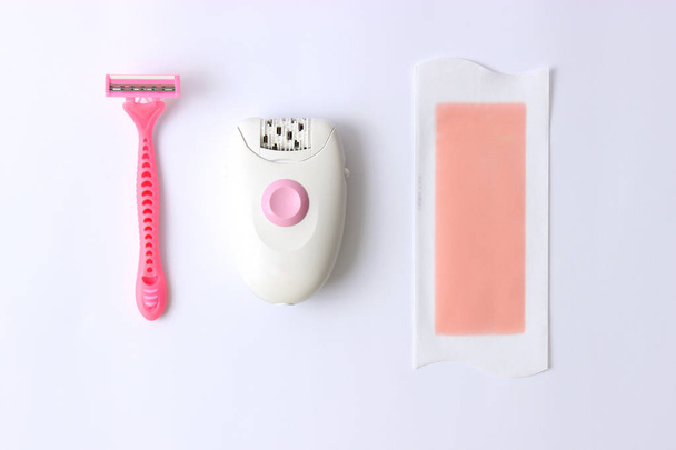 a set of different tools for hair removal on a light background. Removal of unwanted hair. a modern epilator, a razor, wax strips. minimalism, top view, flatlay  - Фото, изображение
