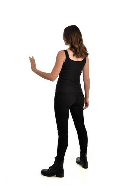 портрет дівчини брюнетки в чорному синглі, джинсах і чоботях. стоїть поза, звернений від камери. ізольовані на білому студійному фоні
. - Фото, зображення