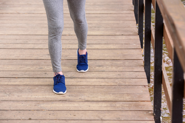 cropped view of sportswoman in sneakers walking on wooden path  - Fotó, kép