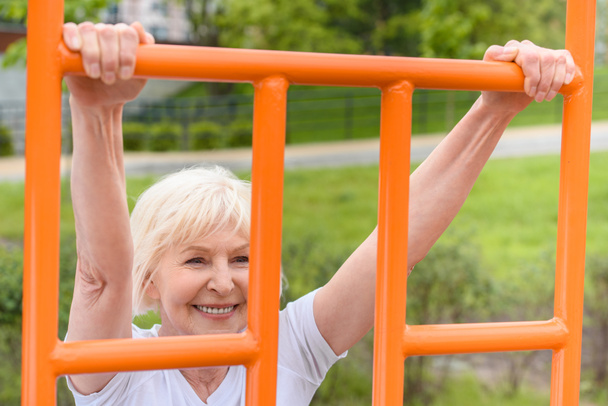 elderly sportswoman with grey hair exercising on sports ground - Foto, afbeelding