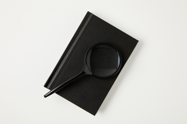 top view of magnifying glass on black notebook isolated on white - Photo, Image