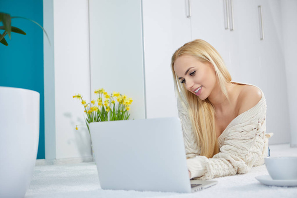 Beautiful woman working on laptop in white bedroom - Фото, изображение