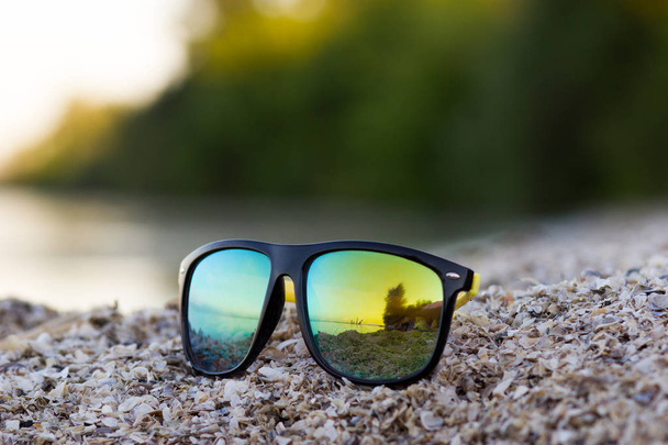 Color sun glasses lie on a beach near the sea shore - Photo, Image