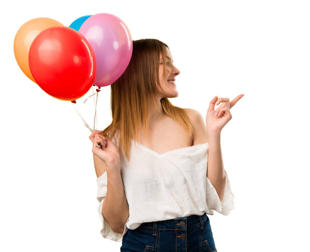 Beautiful young girl holding a balloon and pointing to the lateral - Photo, Image