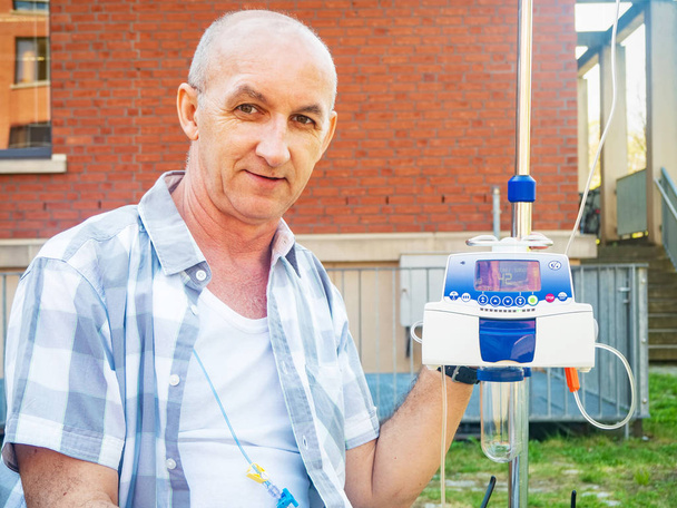 Paciente em tratamento quimioterápico Bomba de infusão IV gotejamento, homem com doença oncológica, terapia oncológica, sorrindo ao ar livre
 - Foto, Imagem