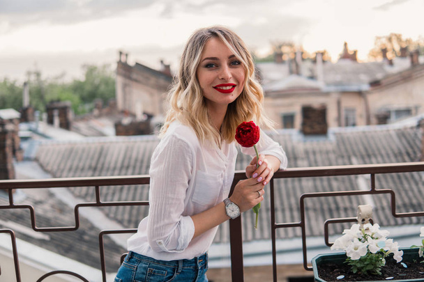 Giovane ragazza allegra tiene fiore rosso sul balcone o sul tetto
 - Foto, immagini