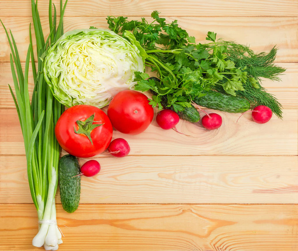 Top view of different fresh vegetables and greens laid out left and top  on a light colored wooden surface and empty remaining part - Photo, Image