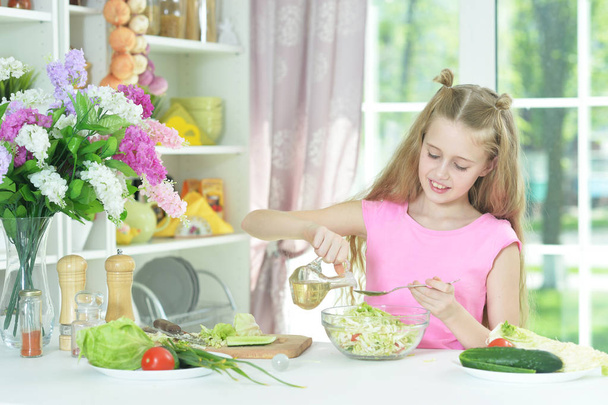 Cute girl preparing delicious fresh salad in kitchen - Фото, изображение