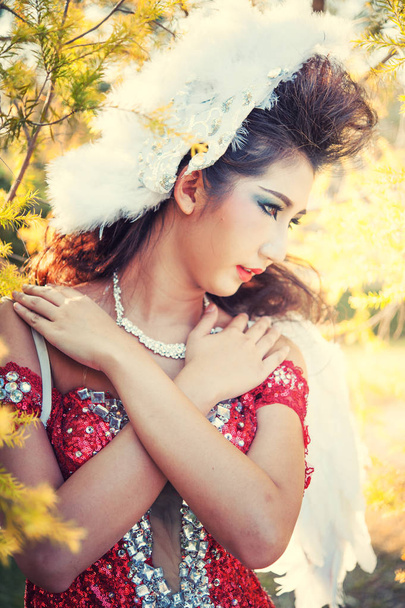 schöne junge Frau mit weißen Winkelflügeln aus rotem Kleid posiert im Garten - Foto, Bild