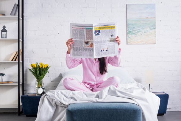 obscured view of woman in pajamas with newspaper in bed at home - Foto, Bild