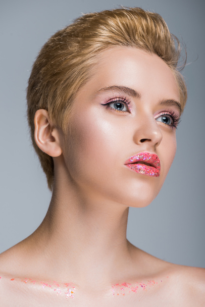 low angle view of attractive woman with glitter on lips and body looking away isolated on grey - Photo, image