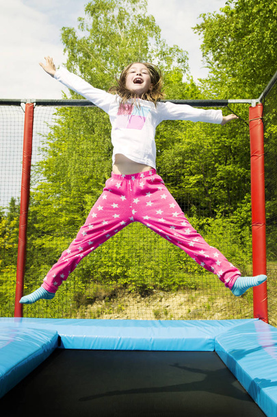 glückliches Mädchen, das an einem sonnigen Tag im Freien hoch auf einem Trampolin springt. - Foto, Bild