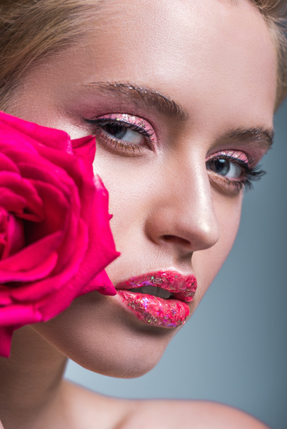 jolie femme avec des paillettes sur les lèvres tenant rose rouge et regardant la caméra isolée sur gris
 - Photo, image