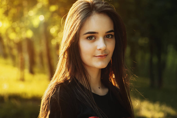 Schönes Nahaufnahme-Porträt eines jungen kaukasischen Mädchens, das im Sonnenuntergang lächelnd in die Kamera blickt. - Foto, Bild