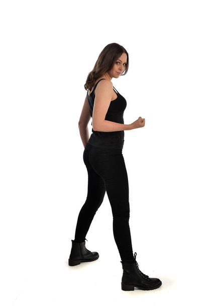 Portret van de volledige lengte van brunette meisje dragen zwart singlet, jeans-jeans en laarzen. staande pose. geïsoleerd op witte studio achtergrond. - Foto, afbeelding